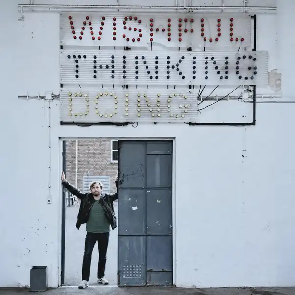 Sjak Meerveld in een deuropening onder een lichtbord met de woorden Wishful Thinking Doing